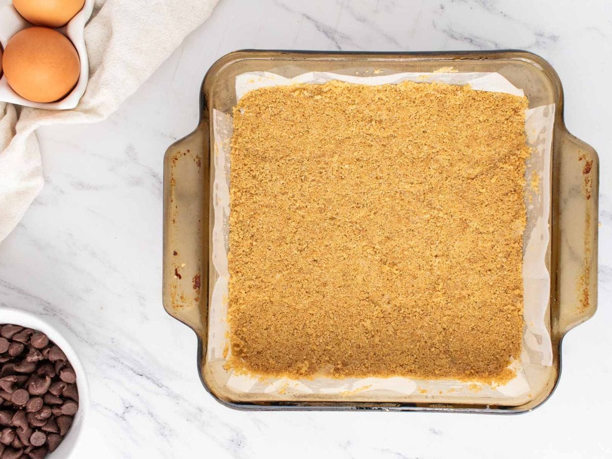 Graham cracker crust in the bottom of a baking pan lined with parchment.