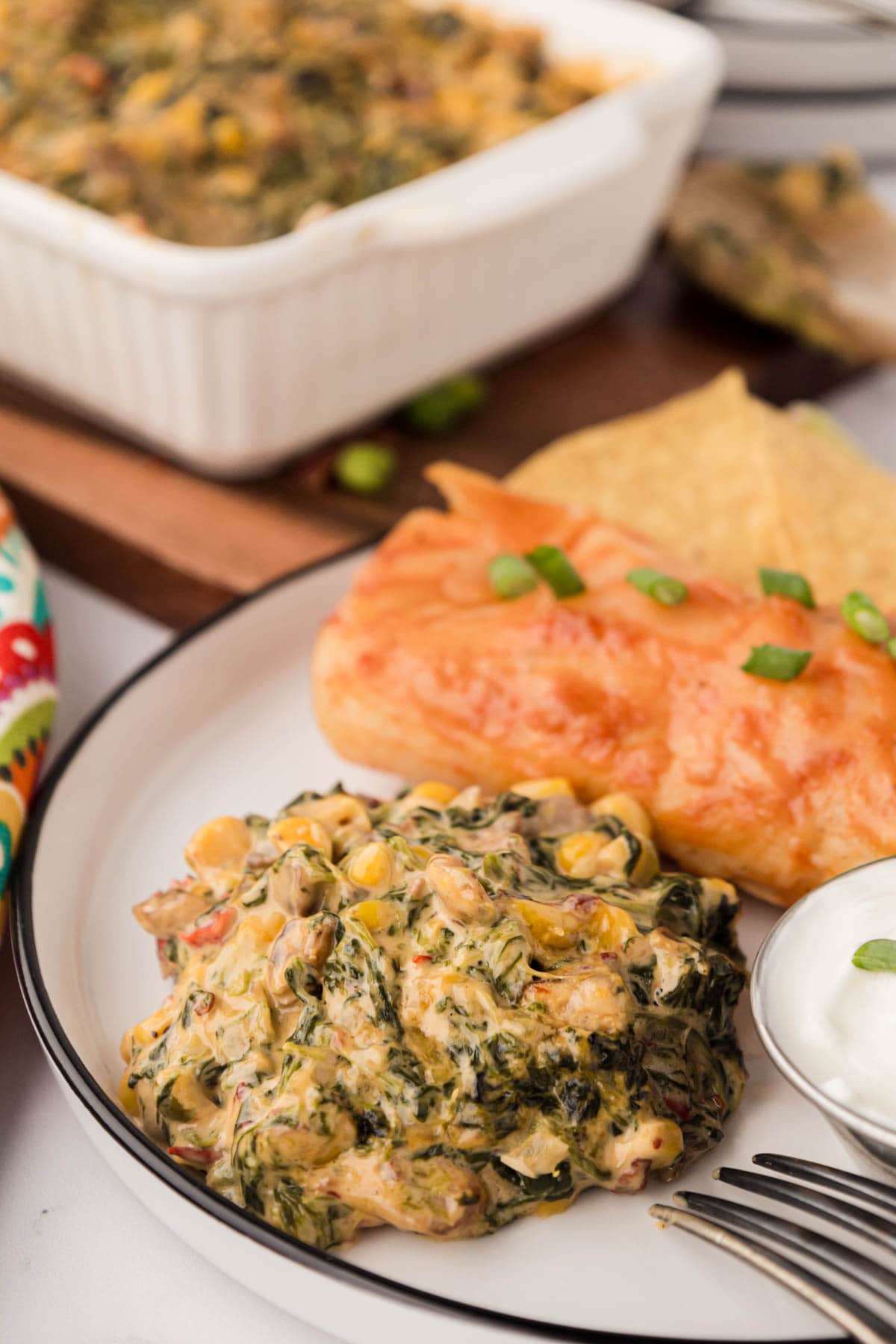 A scoop of creamy mexican spinach on a plate with an enchilada.