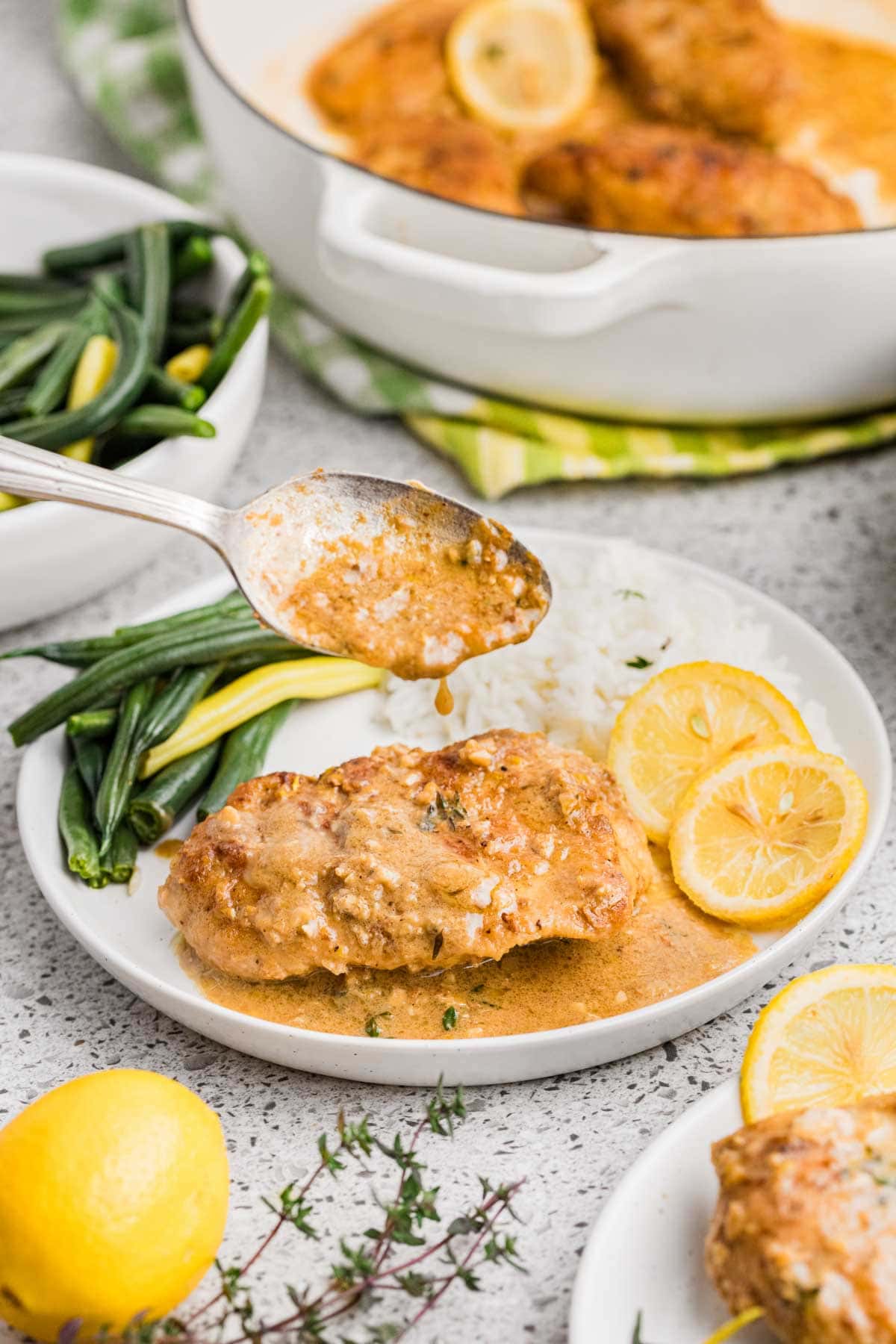 Spooning the lemony butter sauce on top of the chicken served on a plate with sides.