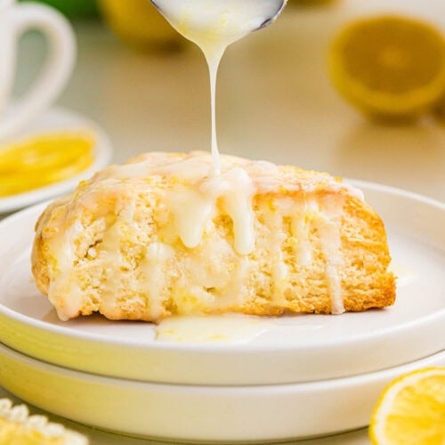 Spooning the lemon glaze on top of a lemon cream scone on a plate.