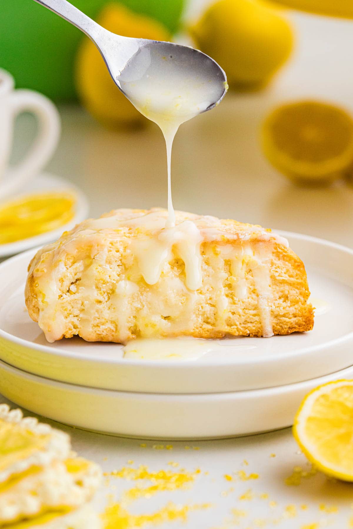 Spooning the lemon glaze on top of a lemon cream scone on a plate.