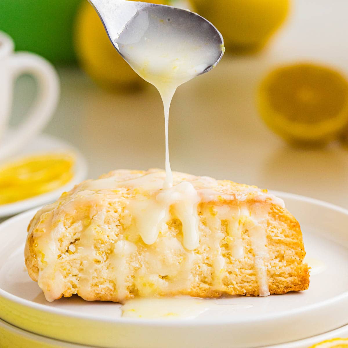 Using a small spoon to drizzle the glaze on a lemon cream scone on a plate.