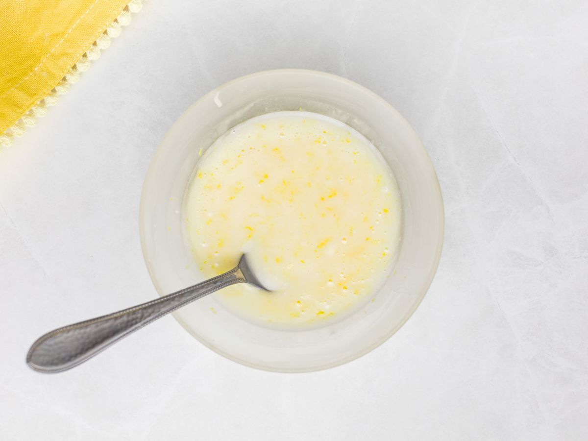 Heavy cream mixed with lemon juice and lemon zest in a small bowl.