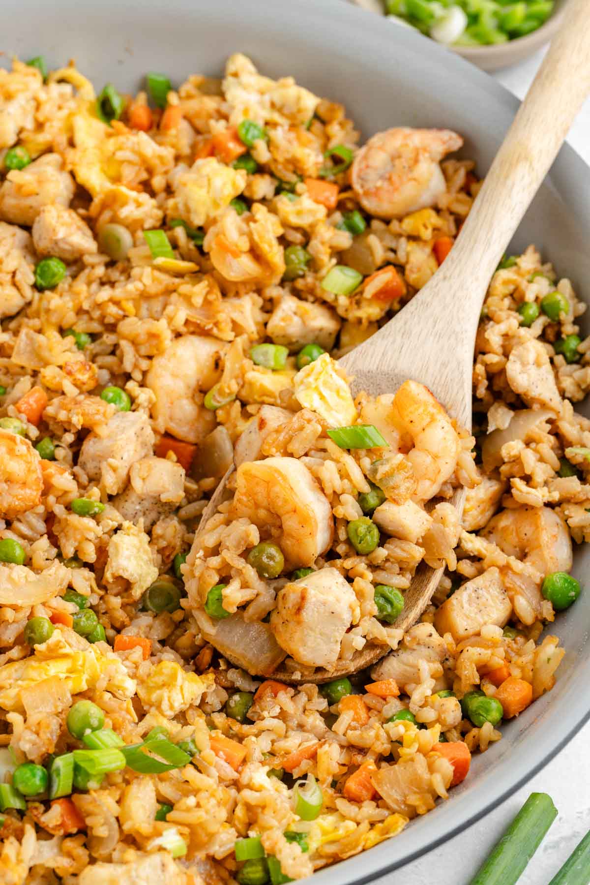 A wooden spoon scooping up a serving of  fried rice with shrimp and chicken.