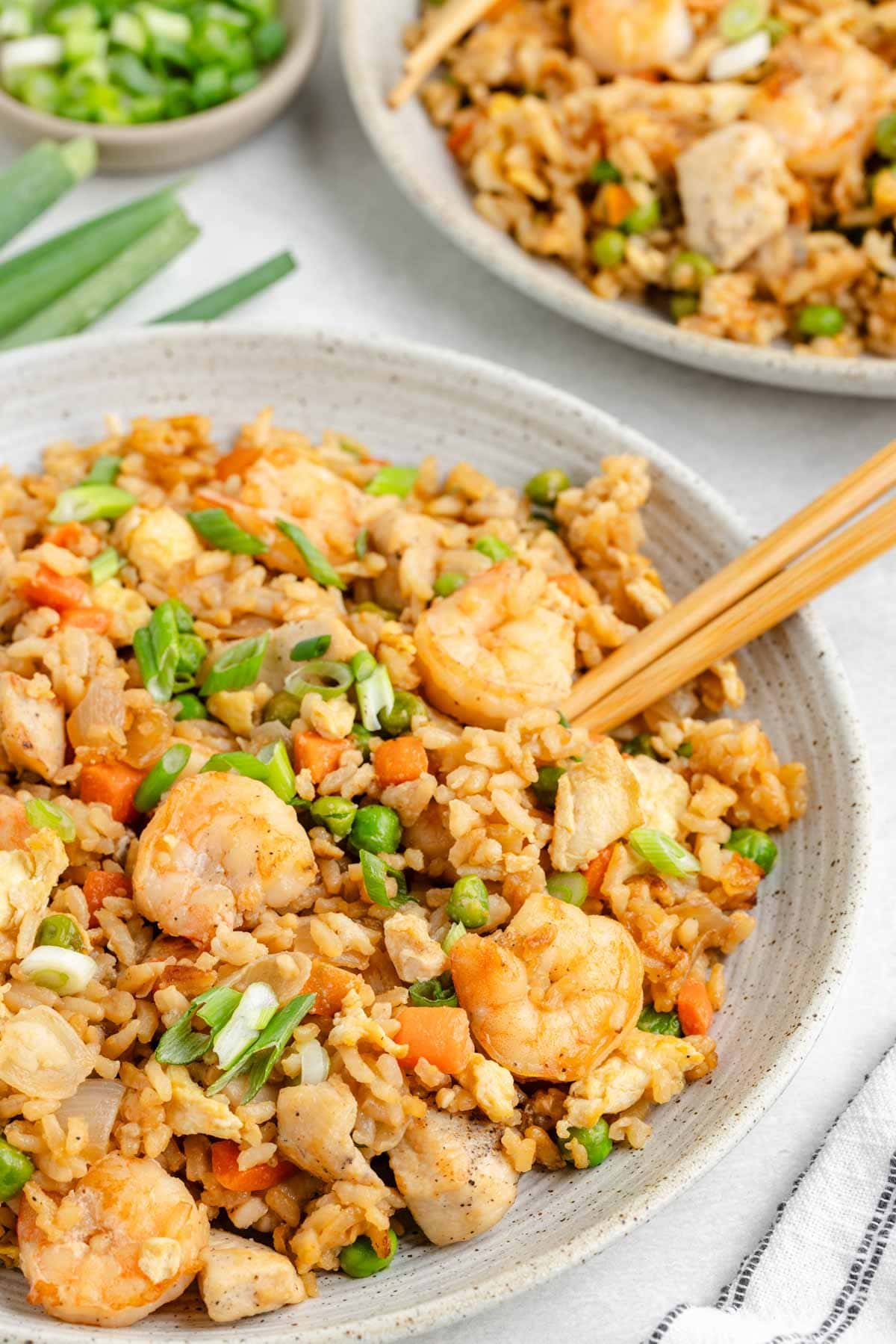 Chopsticks in a bowl of fried rice with chicken and shrimp.