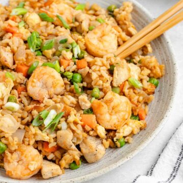 Chopsticks in a bowl of fried rice with chicken and shrimp.