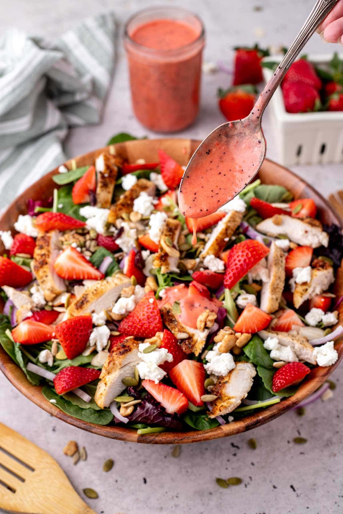 Drizzling the strawberry poppy seed dressing on top of the salad in a wooden bowl.