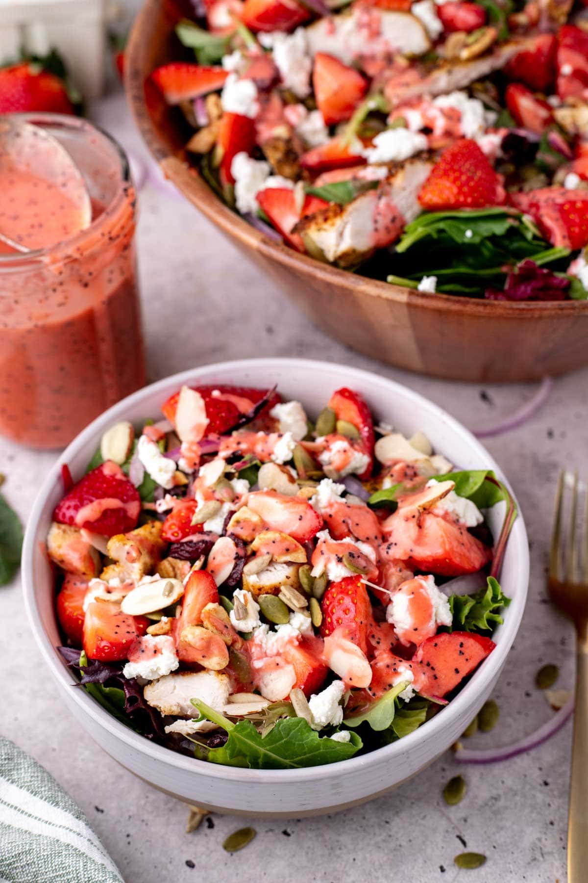 Strawberry poppy seed salad served in a white bowl with the rest of the salad behind it.