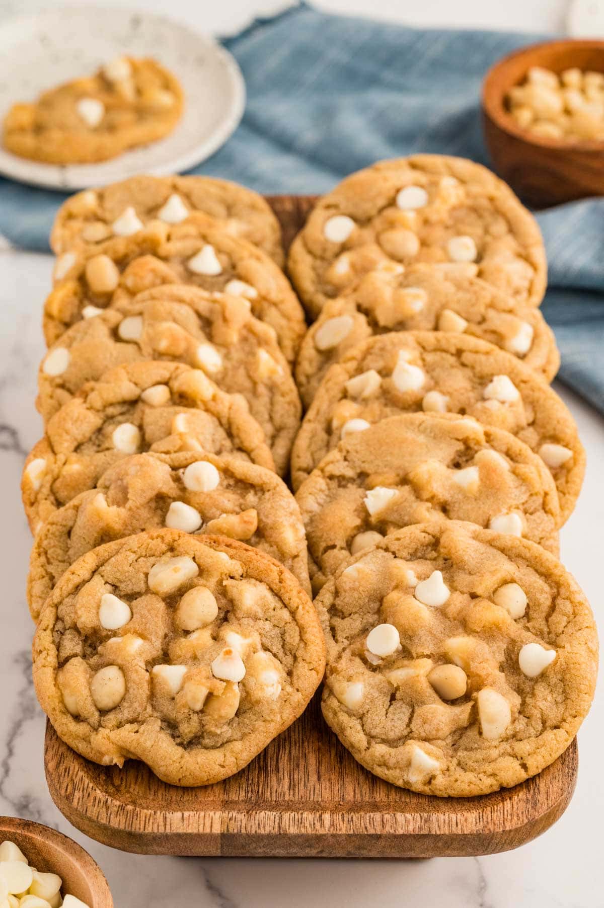 White chocolate macadamia nut cookies lined up against each other on a wooden board.