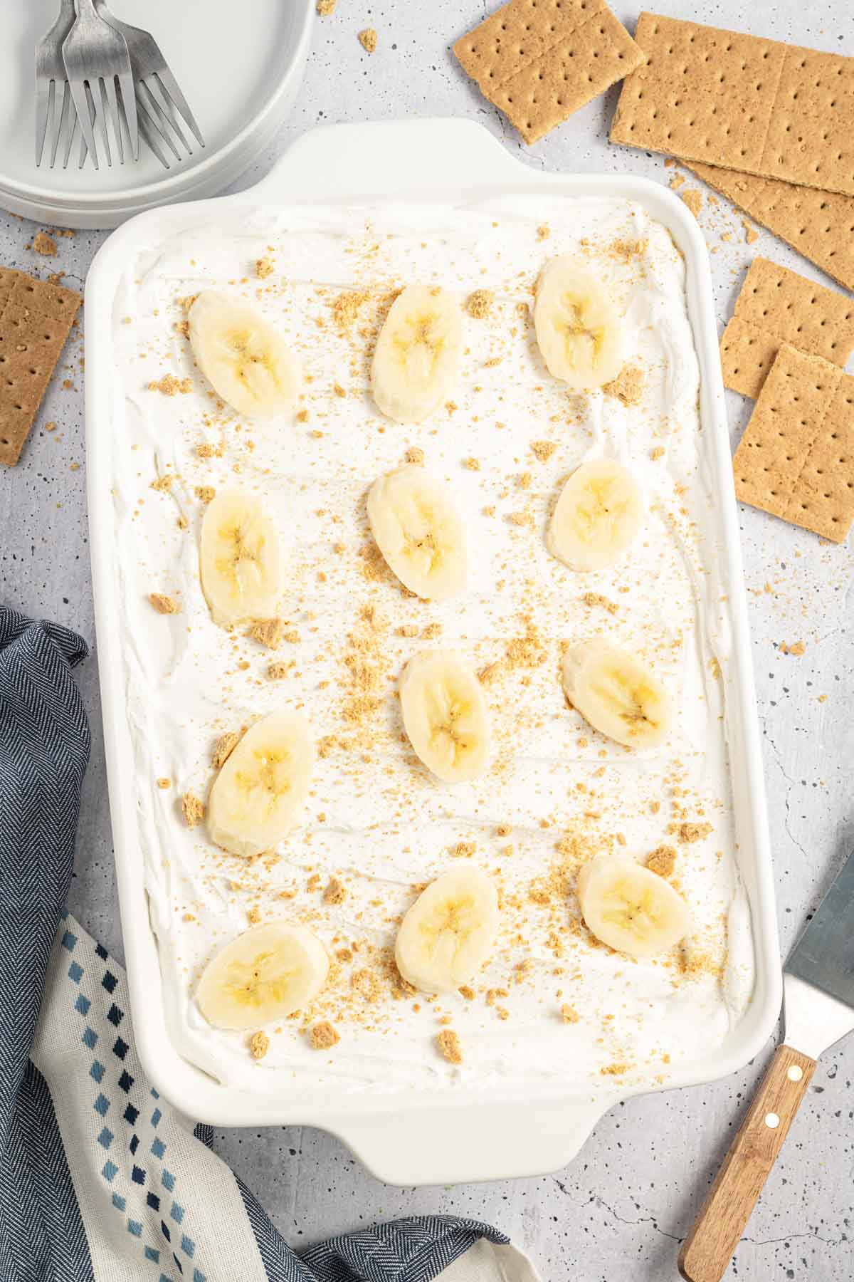 Overhead shot of banana icebox cake in a white baking dish topped with banana slices and graham cracker crumbs.