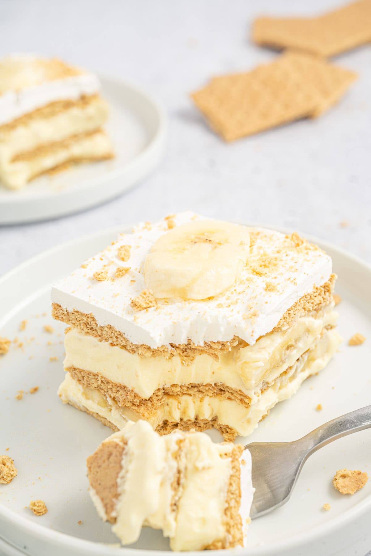 Slice of banana icebox cake on a white plate with a fork taking a bite.