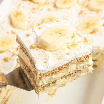 Slice of banana icebox cake on a metal spatula topped with a slice of fresh banana and graham cracker crumbs.