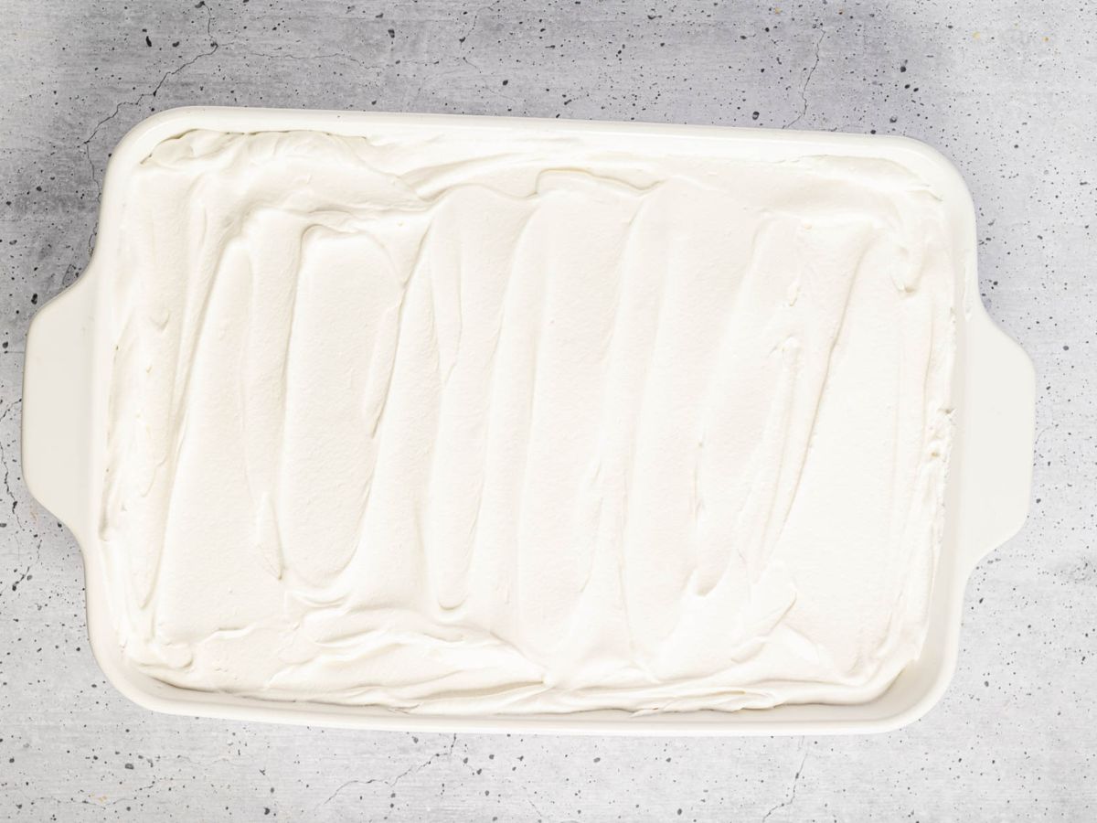 Final layer of whipped topping on top of the banana icebox cake in a baking dish.