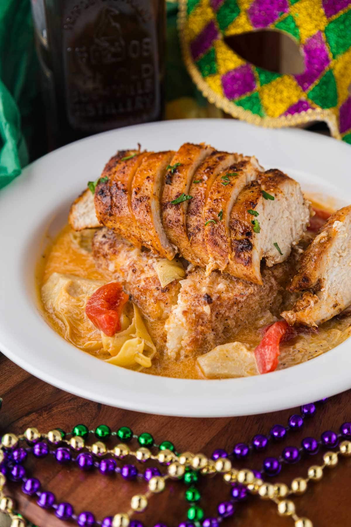 A plate of who that chicken with a Cajun lemon butter sauce with a Mardi Gras mask in the background.