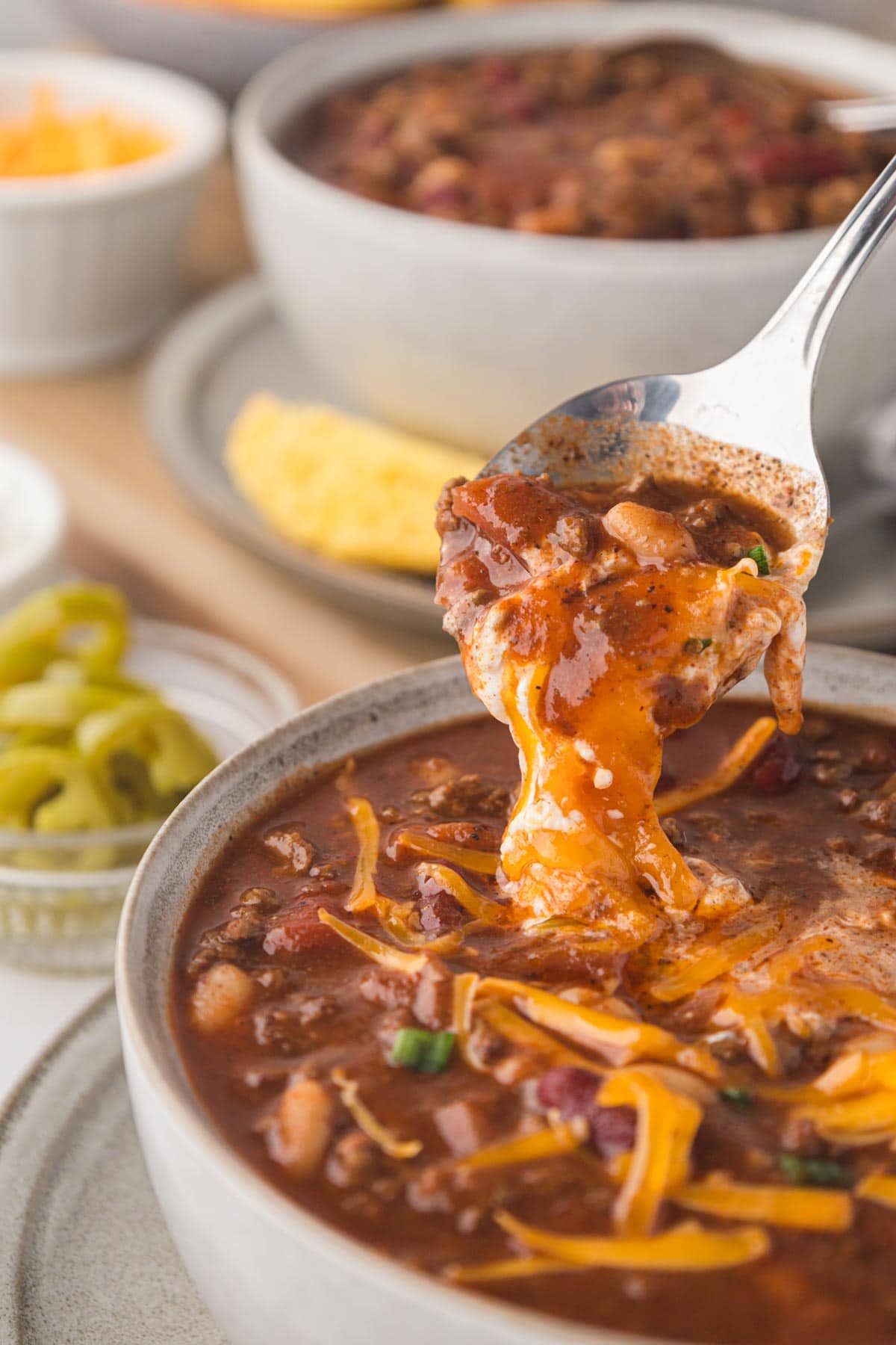 A spoon taking a cheesy bite of chili from the bowl.