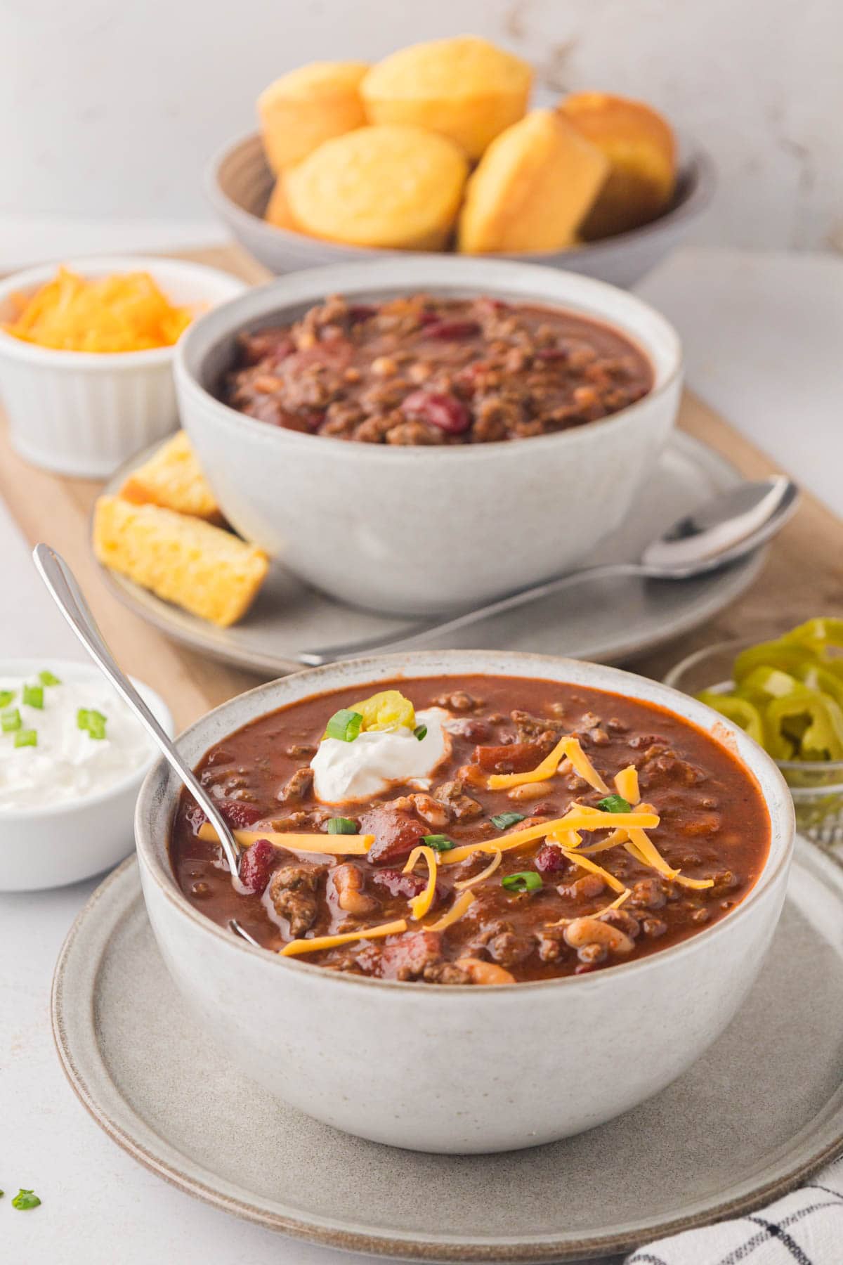 A bowl of chili top with shredded cheese, a dollop of sour cream and sliced green onions.