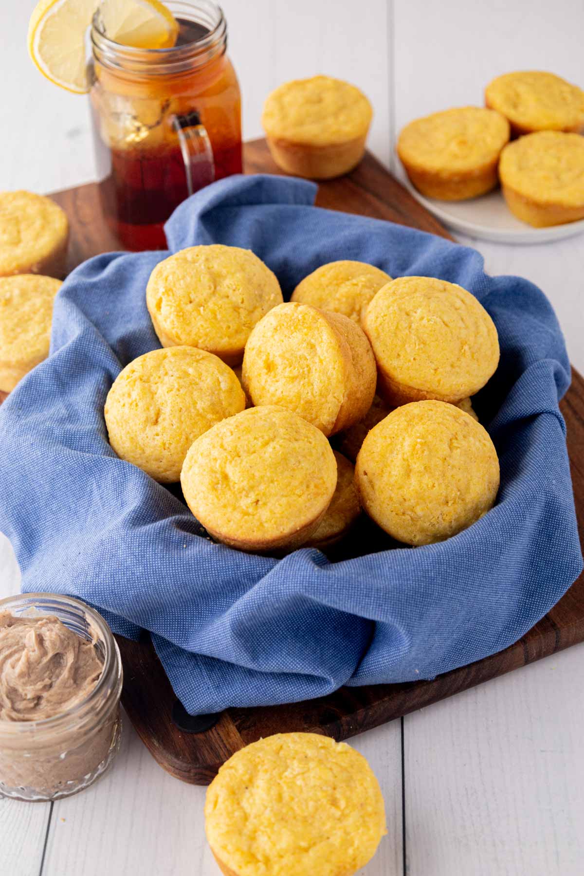 A bread bowl line with a blue cloth filled with cream, corn cornbread muffins.