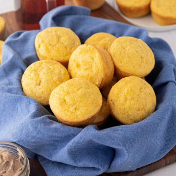 A bread bowl line with a blue cloth filled with cream, corn cornbread muffins.