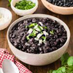 A bowl of cuban black beans, garnished with diced onion and parsley