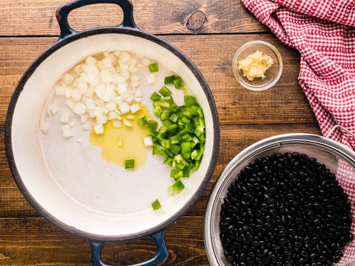 A Dutch oven with oil, diced onion and diced green bell pepper.