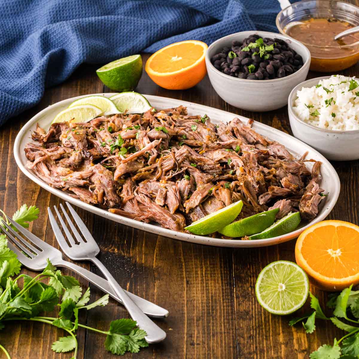 A serving platter with Mojo pork and black beans and rice in the background.