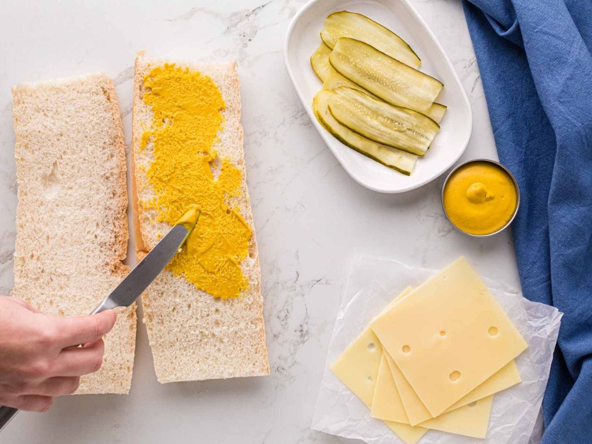 Smearing mustard on cuban bread.