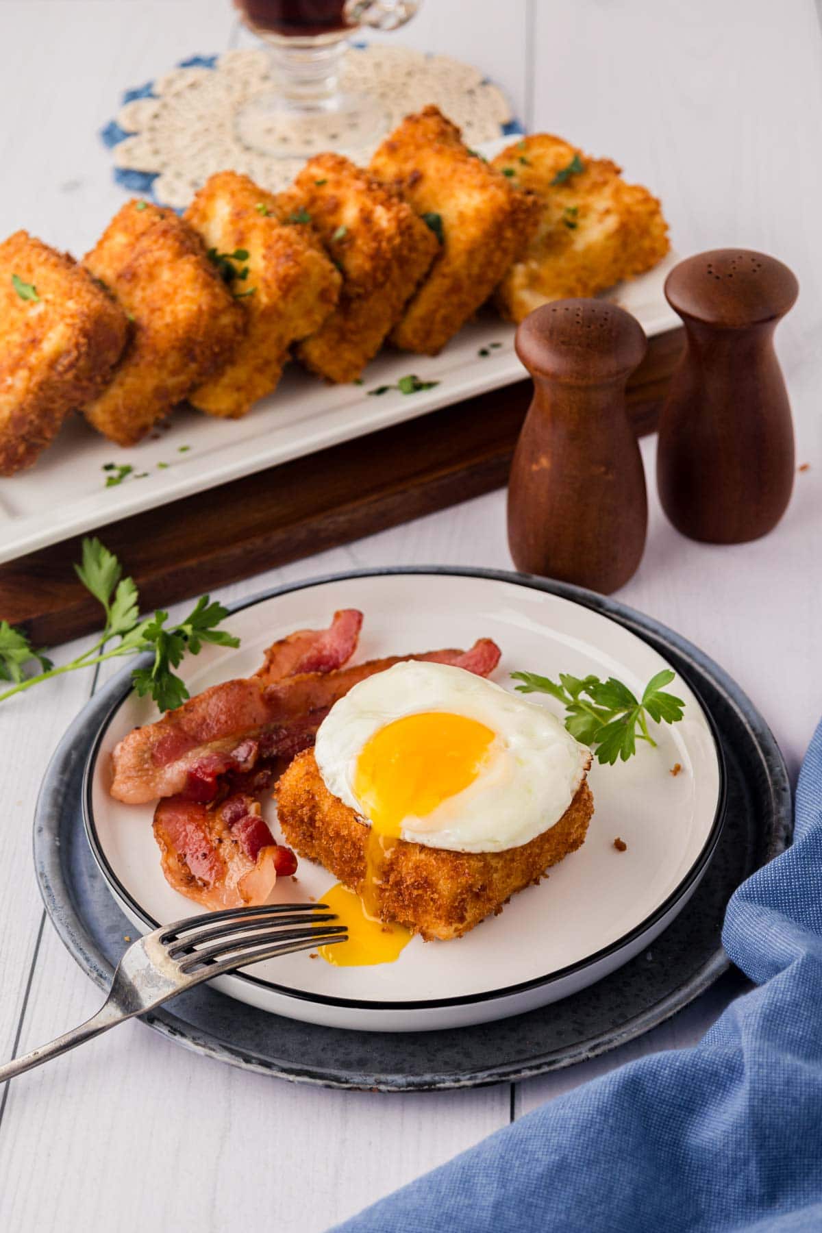 Grit cake topped with a fried egg and a side of sliced bacon on a white plate.