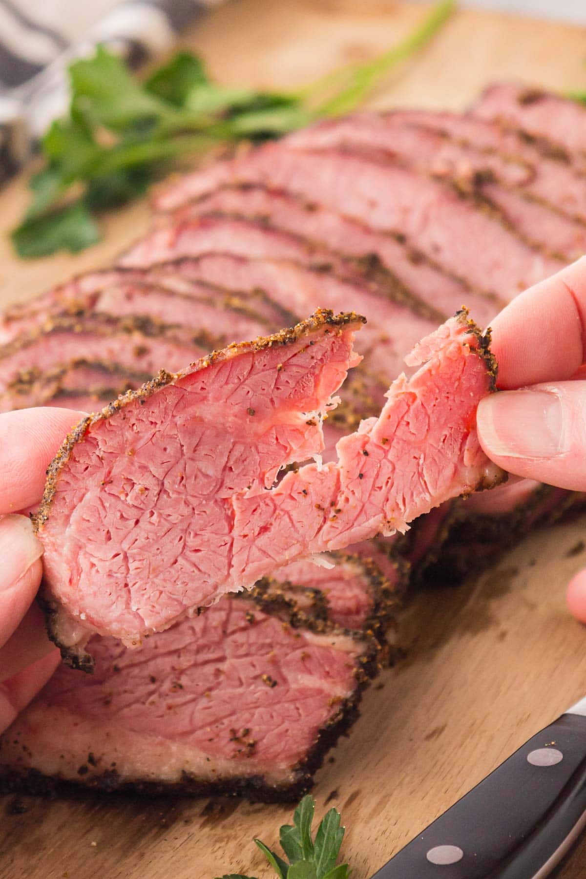 A hand holding a slice of pastrami.