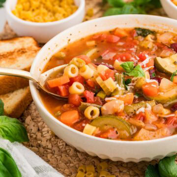 Minestrone soup served in a white bowl with a spoon picking up a bite.