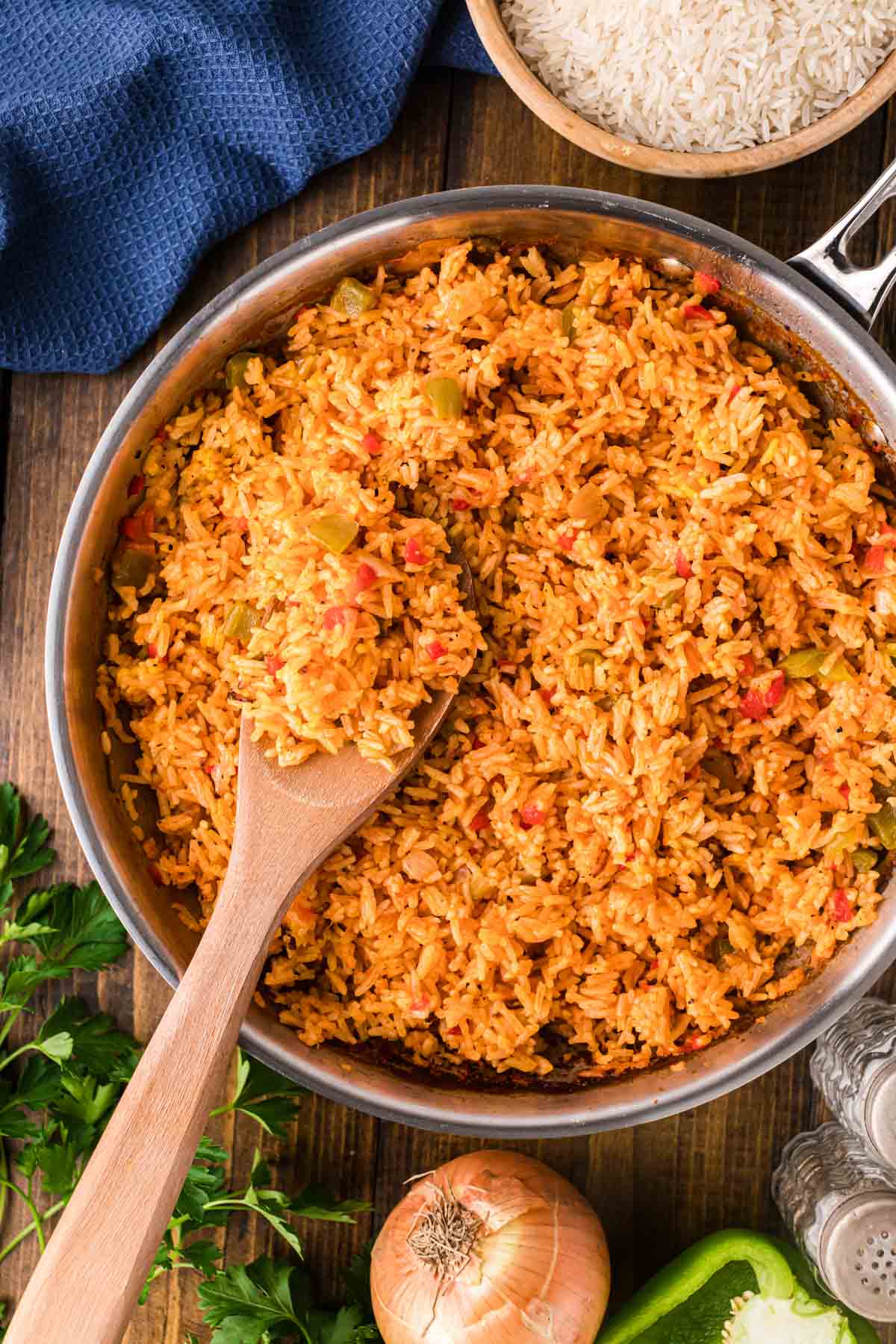 A stainless steel skillet with a wooden spoon, removing a scoop of yellow rice.