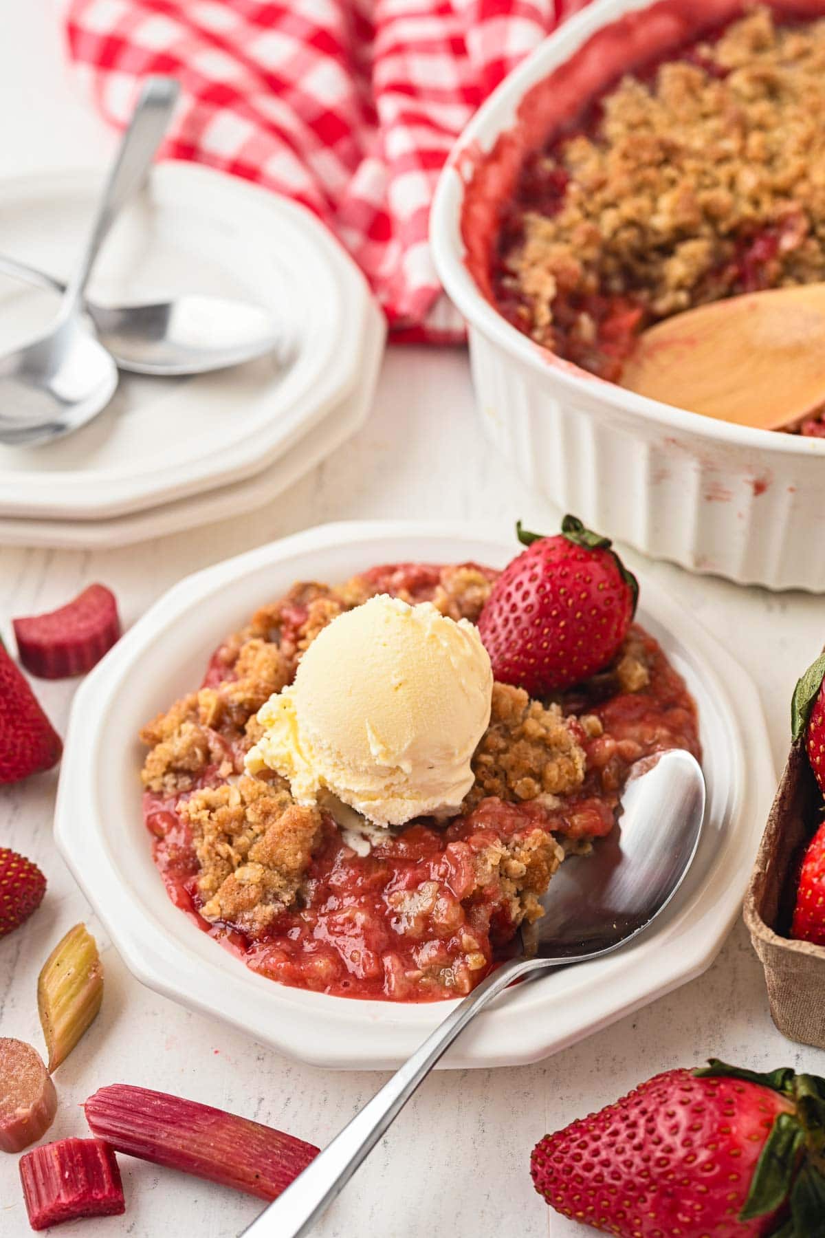 Portion of strawberry rhubarb crumble on a white plate with a scoop of ice cream on top.