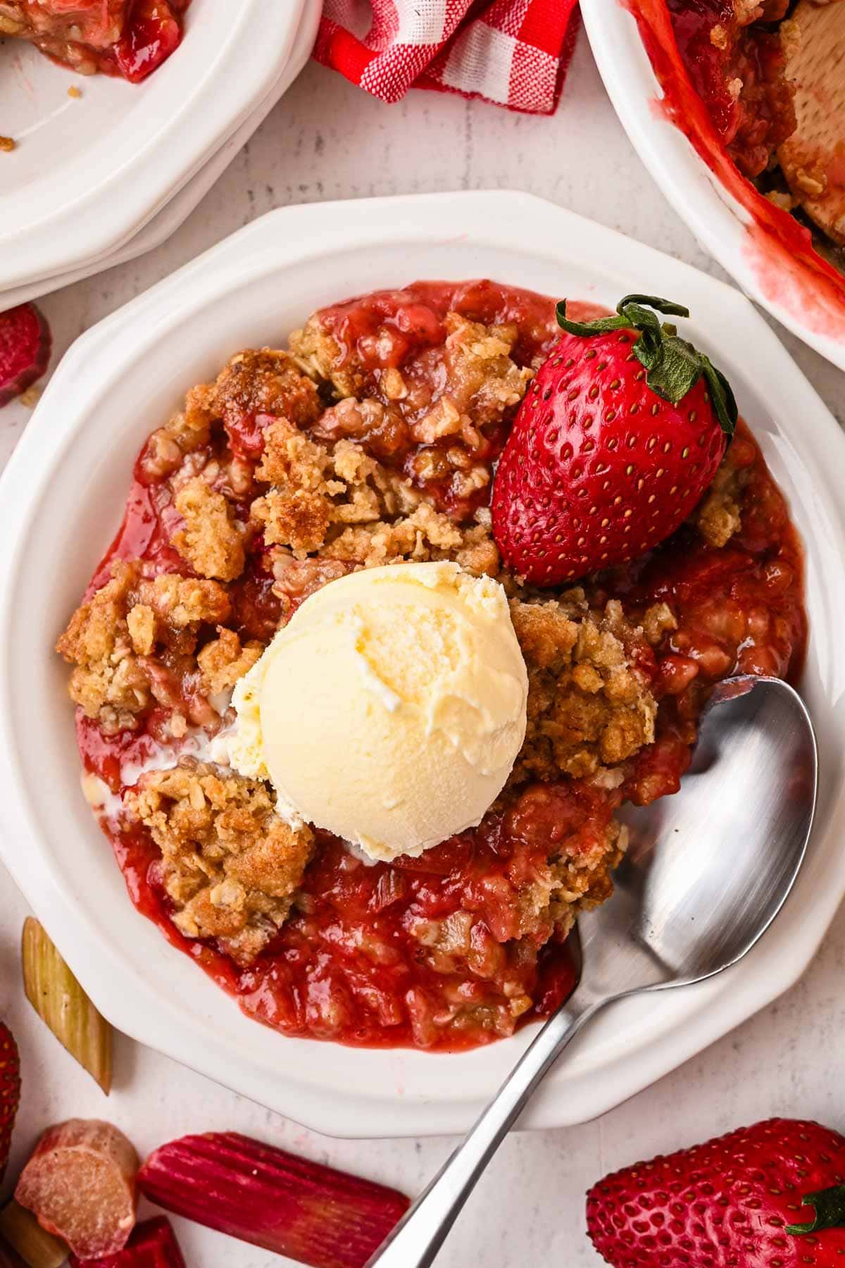 Overhead shot of strawberry rhubarb crumble on a white plate with ice cream on top.