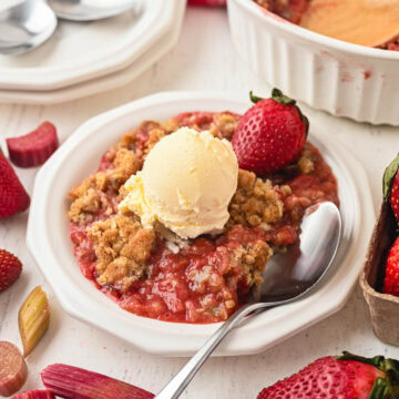 Strawberry rhubarb crumble served on a white plate with a spoon and scoop of ice cream.