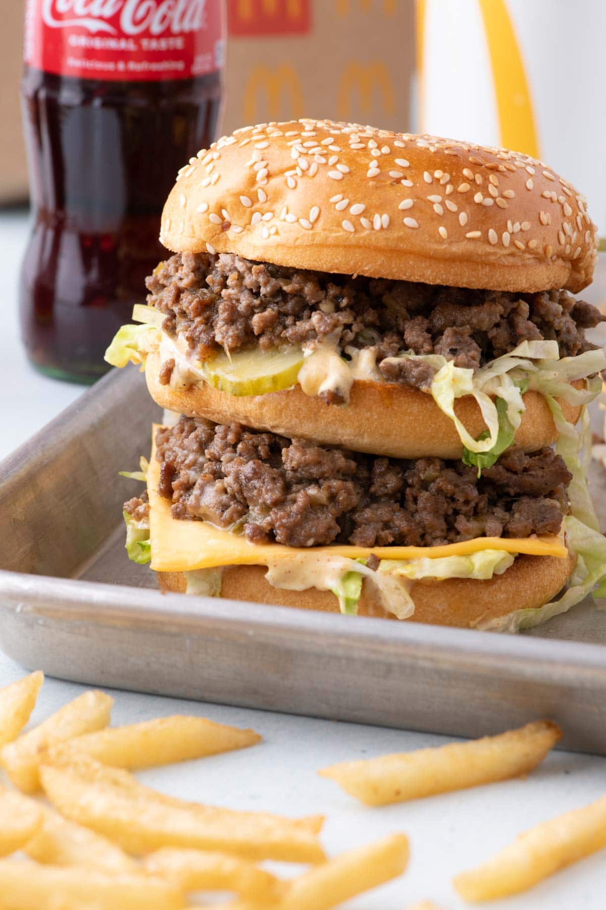 Side view of a big mac sloppy joe on a sheet pan with coke in the background.