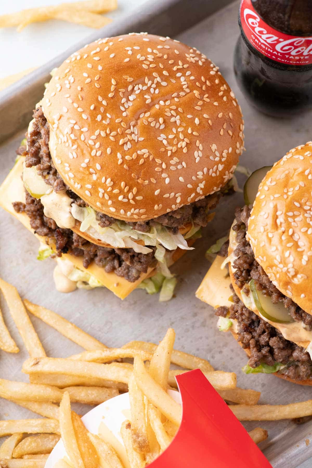 Two big mac sloppy joes on a sheet pan with fries and a coke on the side.