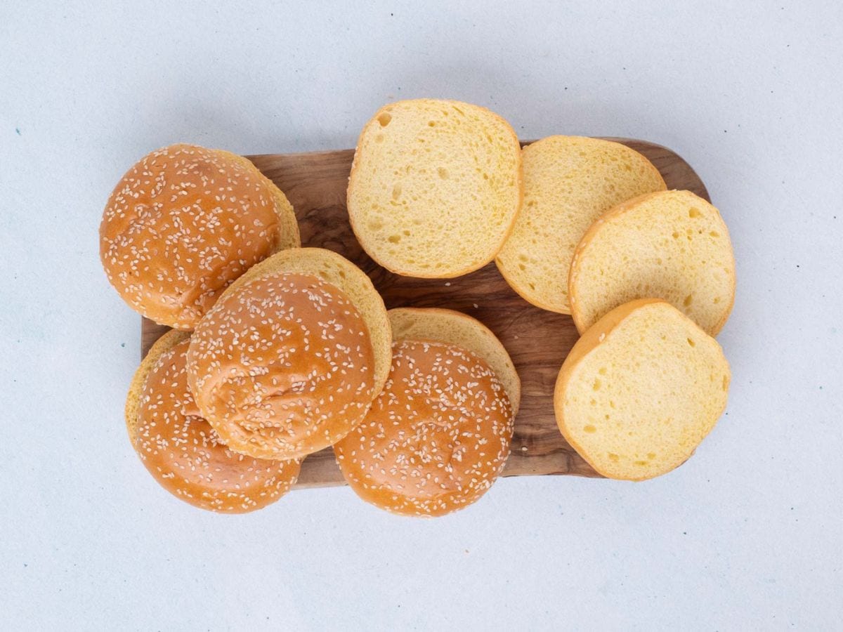 Four full hamburger buns plus four bottom halves of the buns on a wooden board.