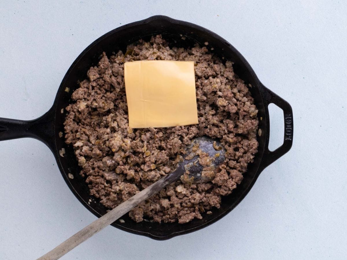 Slice of American cheese added to cooked ground beef.