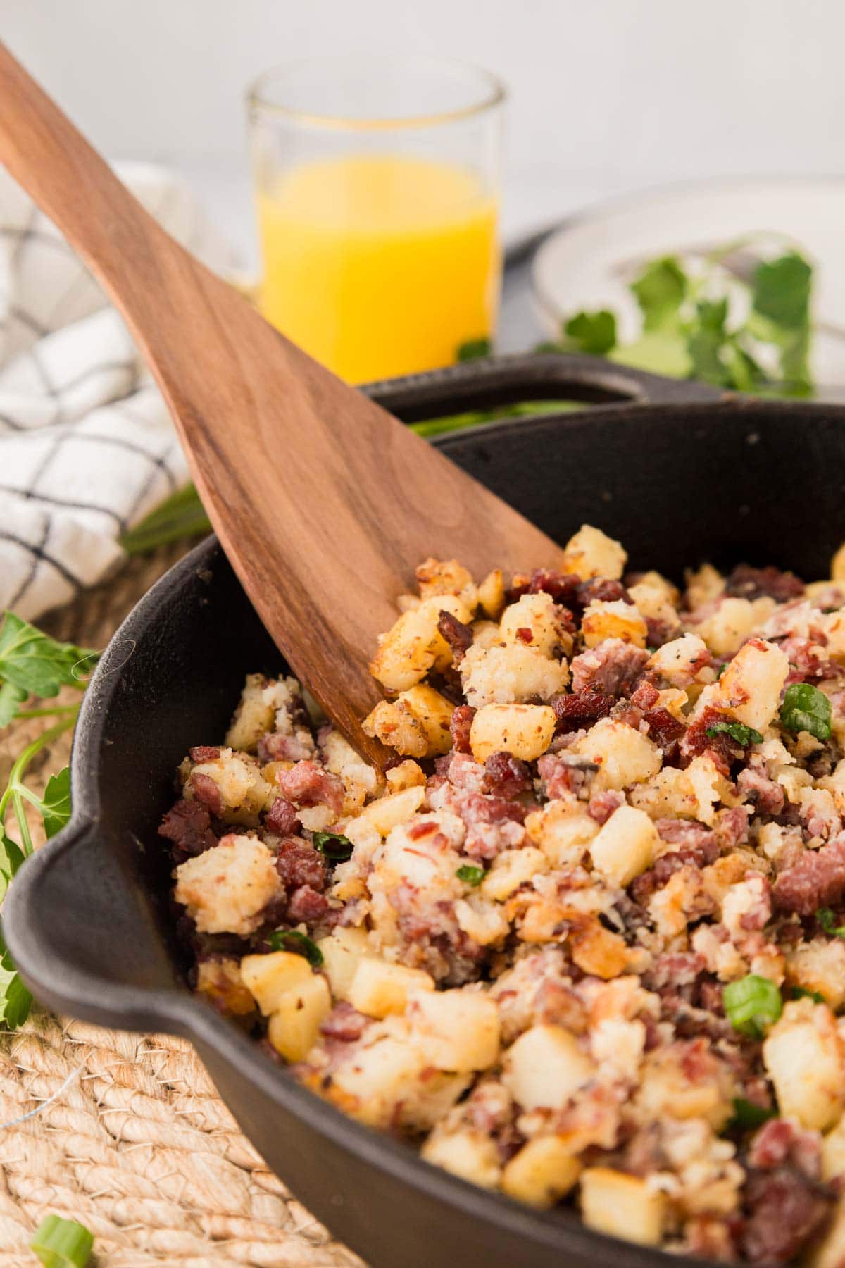 Close up of corned beef has in a cast iron skillet with a wooden spoon.