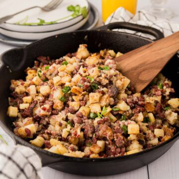 Corned beef has in a cast iron skillet with a wooden spoon and parsley on top.