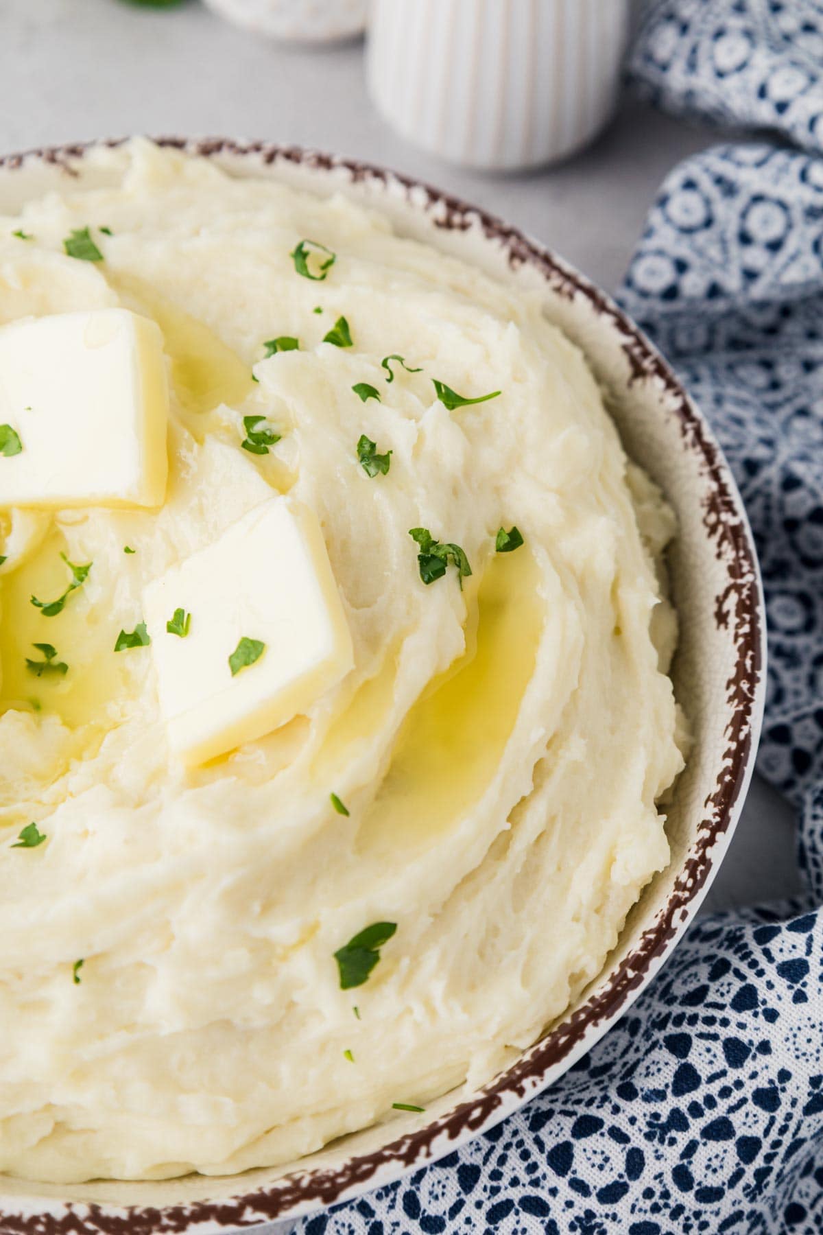 Serving bowl filled with homemade mashed potatoes with butter and parsley on top.