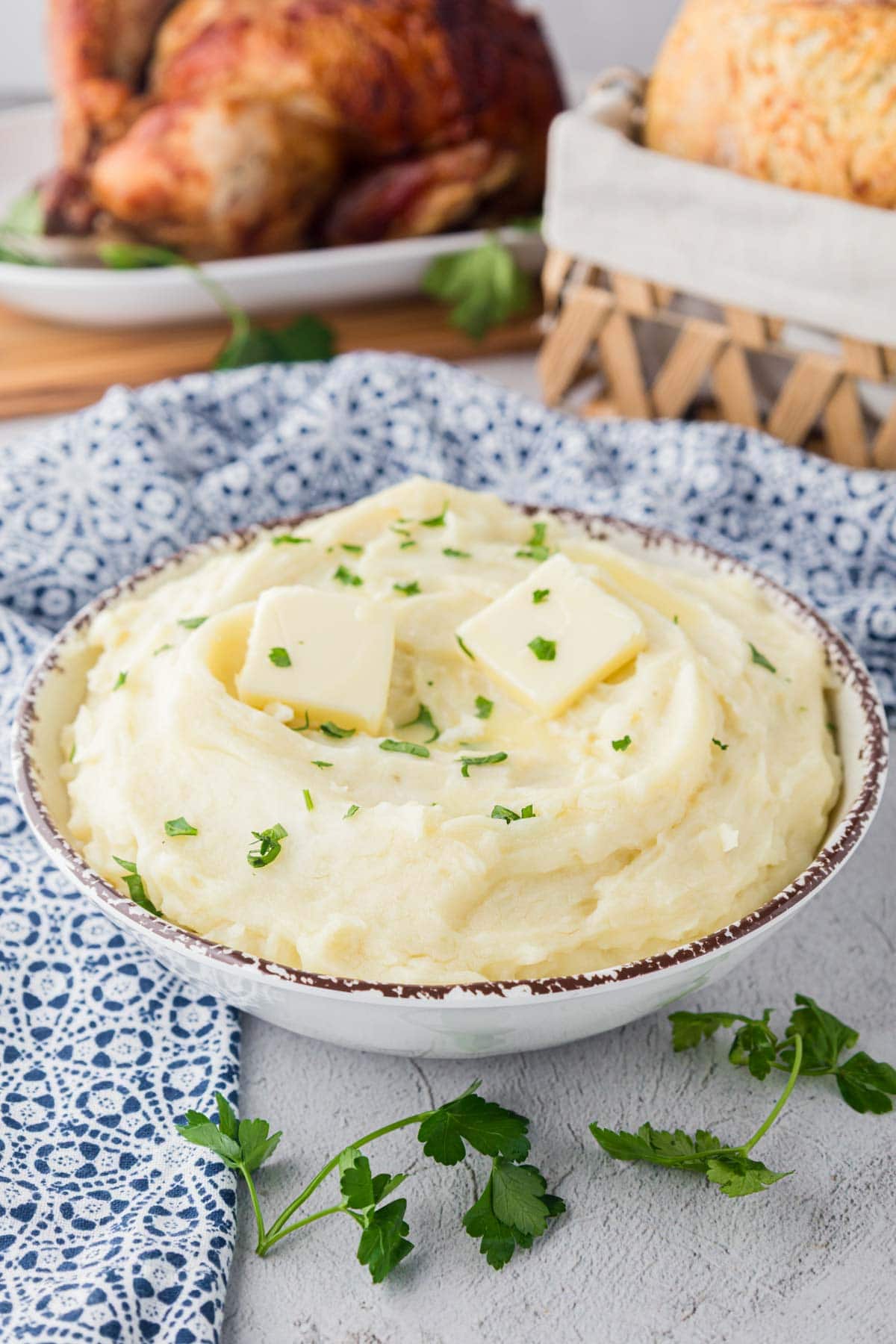 Fluffy homemade mashed potatoes in a serving bowl with pats of butter and parsley on top.