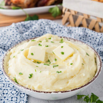 Side view of a bowl of mashed potatoes topped with butter and parsley.