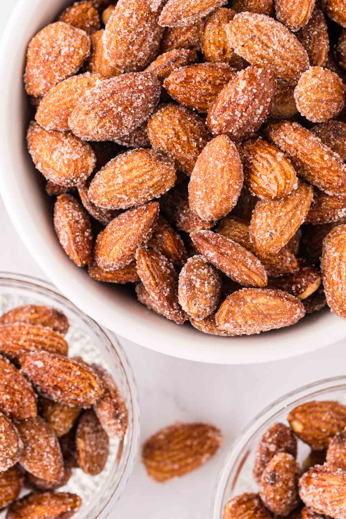 Overhead shot of honey roasted almonds in a white ramekin next to two small glass bowls of almonds.