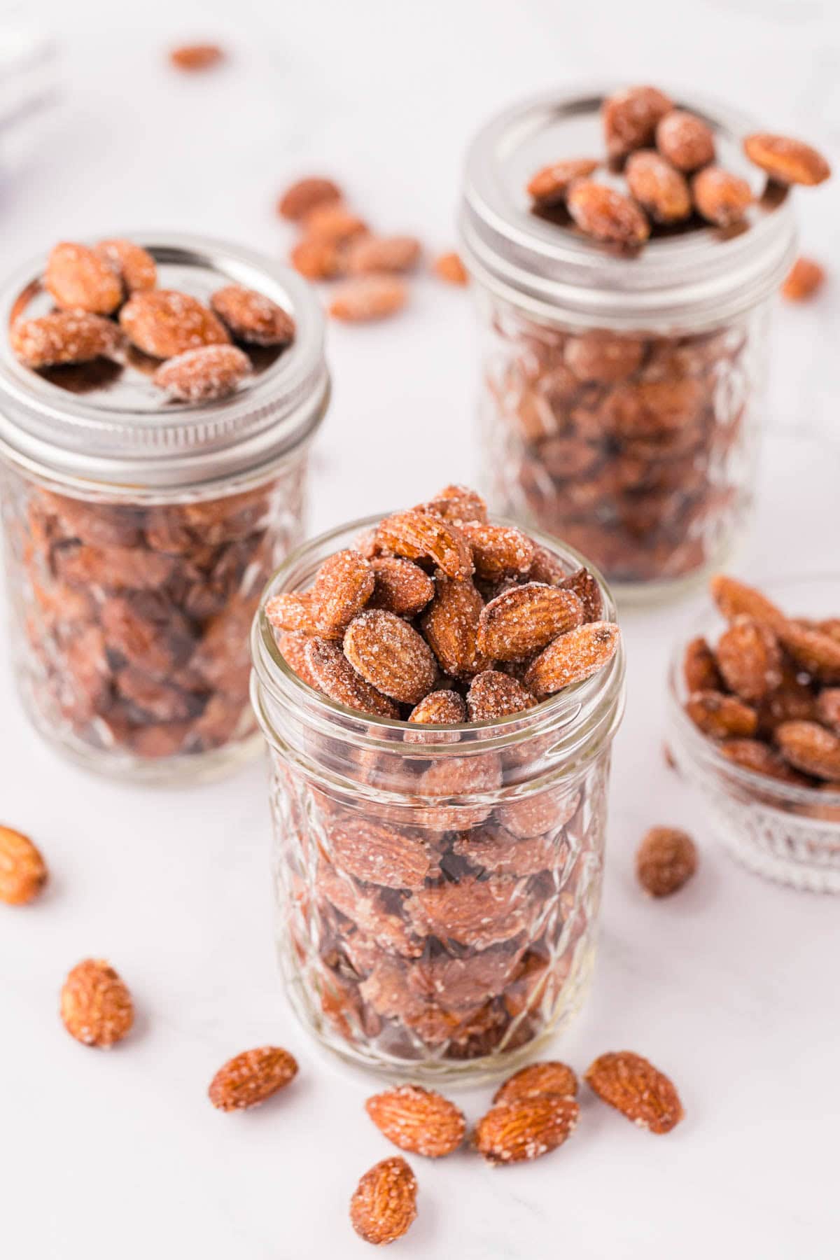 Three jars filled with honey roasted almonds on a white background.