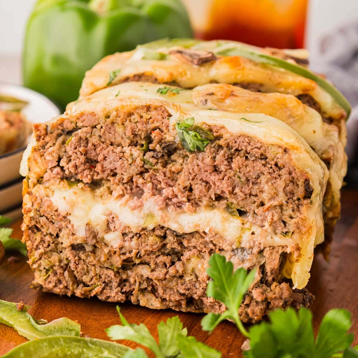 Side view of a slice of Philly cheesesteak meatloaf with a layer of cheese in the middle and on the top.