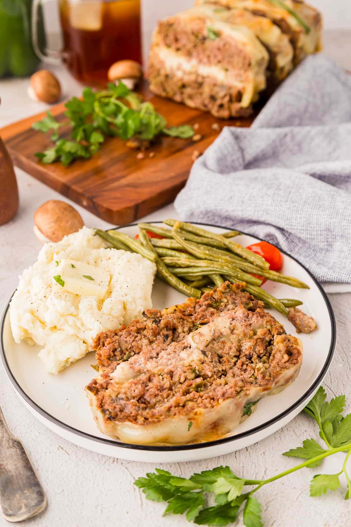 Slice of Philly cheesesteak meatloaf on a plate served with mashed potatoes and green beans.