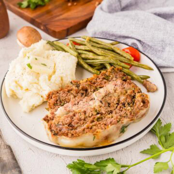 Meatloaf slice served on a plate with green beans and mashed potatoes.