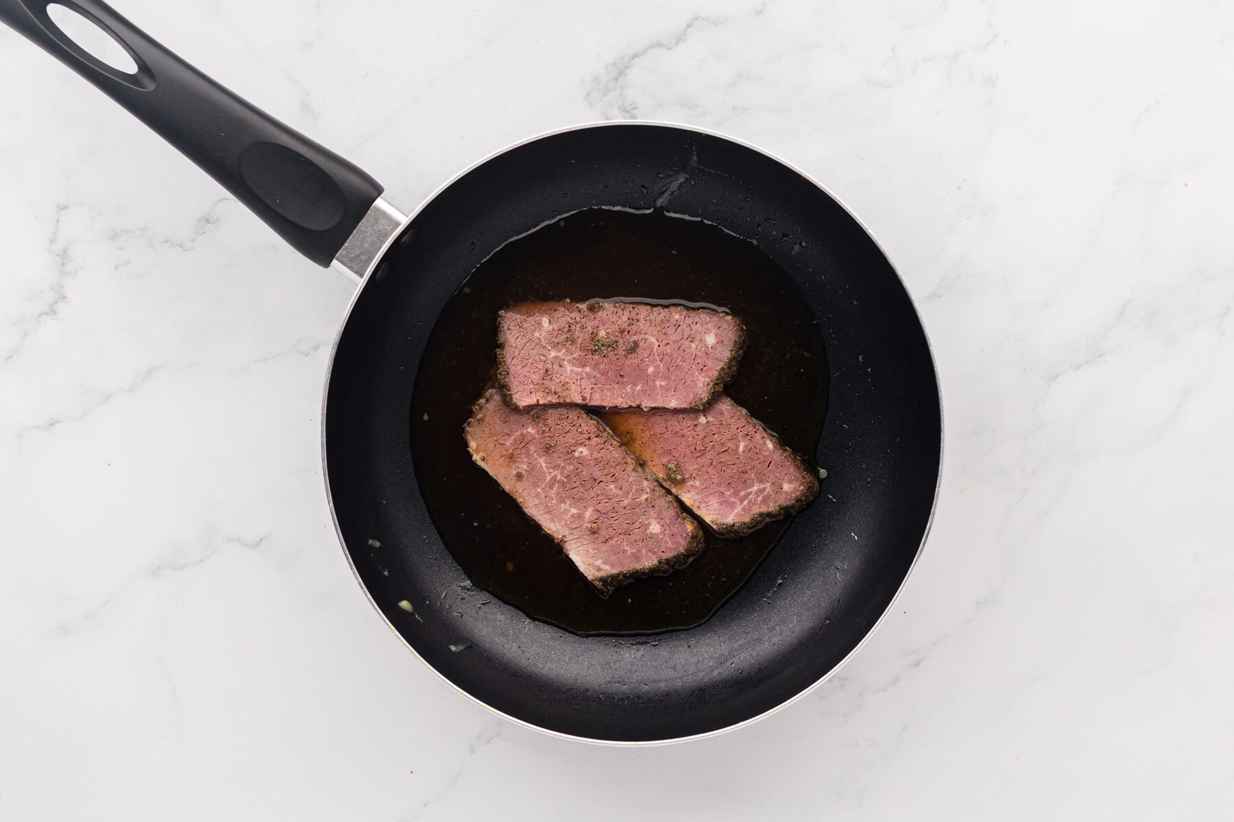 Slices of corned beef in a skillet with cooking liquid.