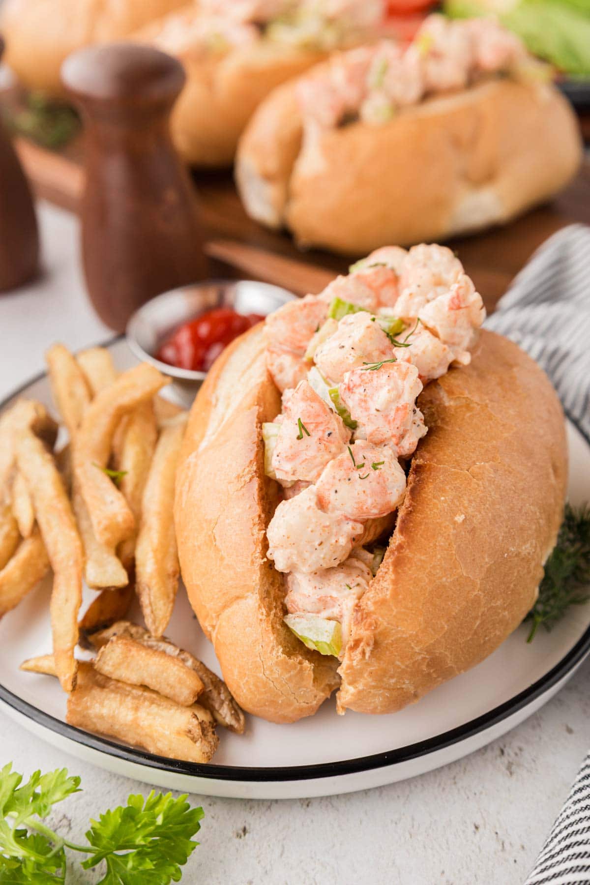 A plate with a shrimp salad sandwich on a bun and french fries.